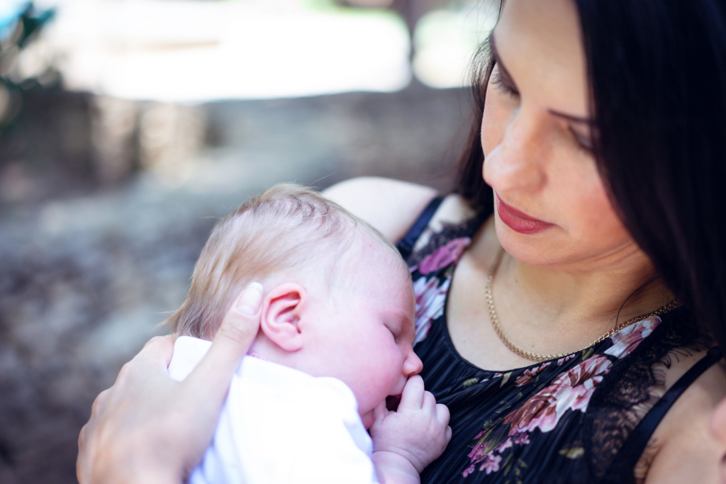Tender moment of a mother holding her sleeping newborn baby outdoors.