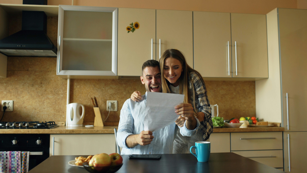 An older couple sitting at a kitchen table looking over financial statements with a calculator and coffee cups