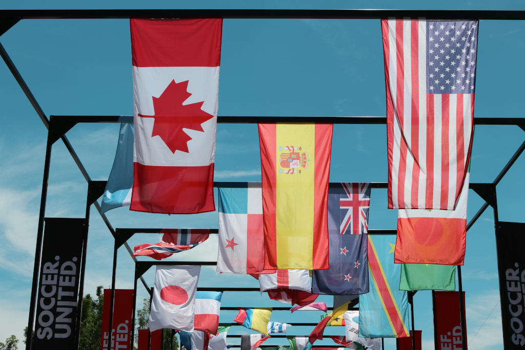 A small American flag and a small Canadian flag mounted side by side outdoors under a blue sky